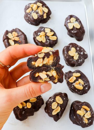 Snickers style chocolate covered dates cut in half in hand on a sheet pan.
