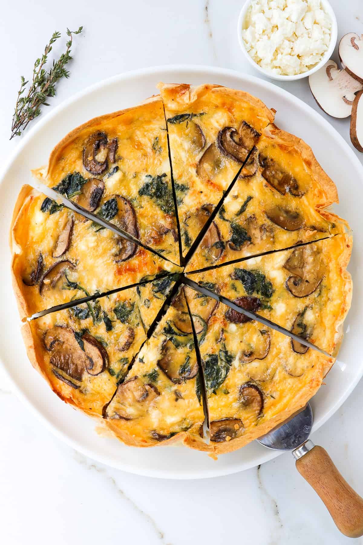 Spinach mushroom quiche on a plate with a wooden spatula.