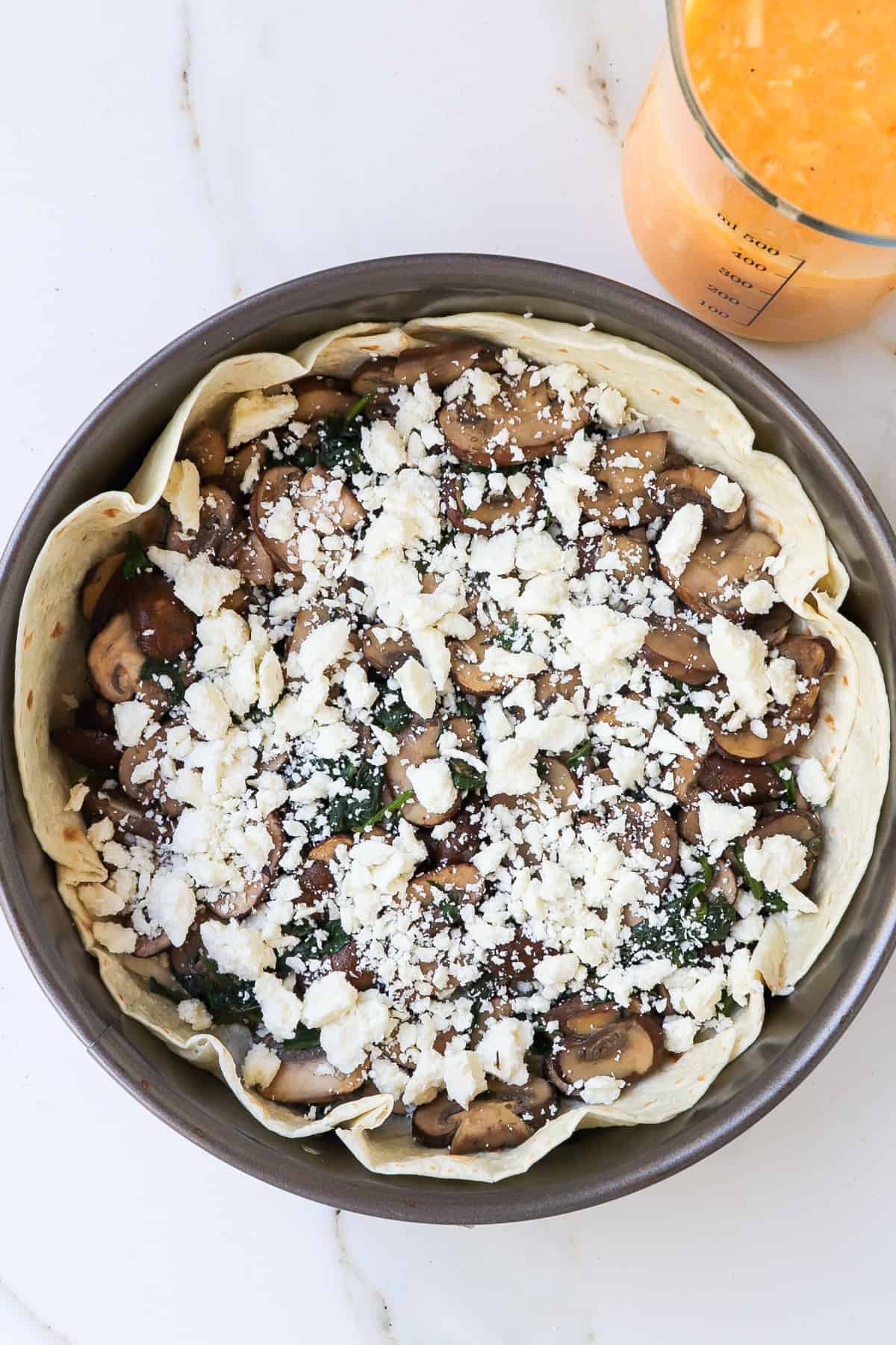 Springform pan with cooked mushrooms and feta in a tortilla shell.
