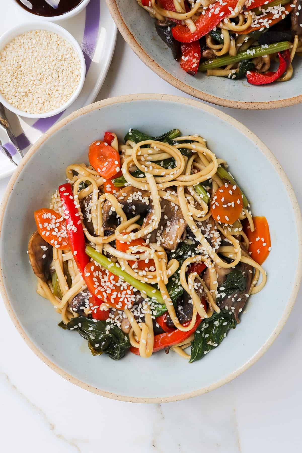 Teriyaki udon noodles with vegetables and sesame seeds in a bowl.