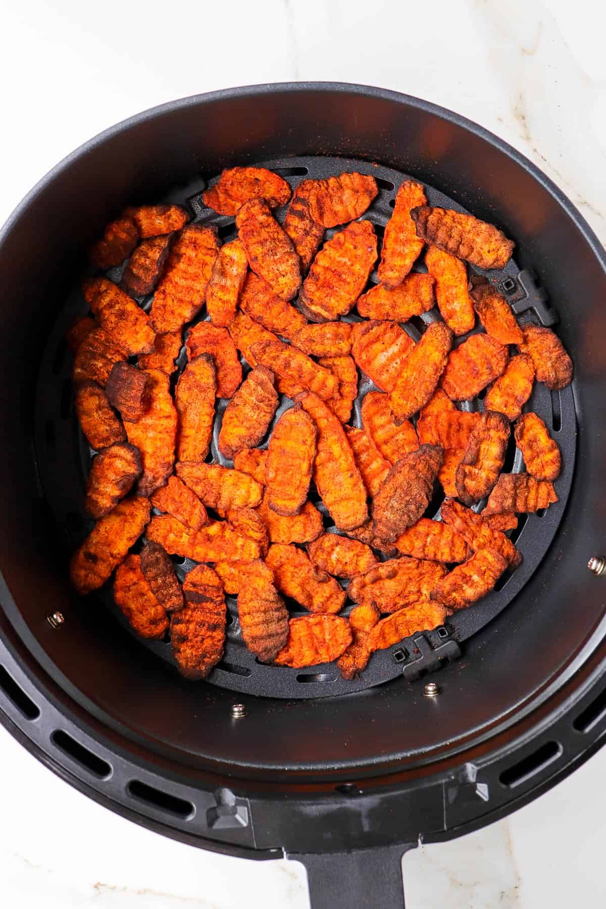 Crispy carrot pieces in air fryer basket.