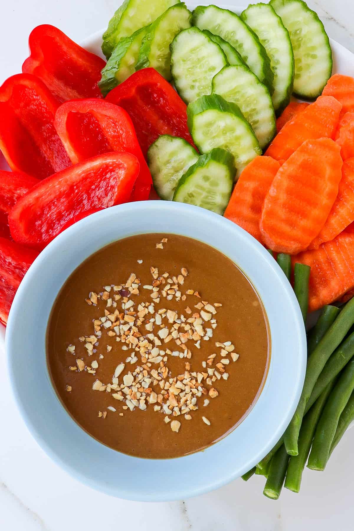Hoisin peanut sauce in a bowl with sliced veggies on the plate.