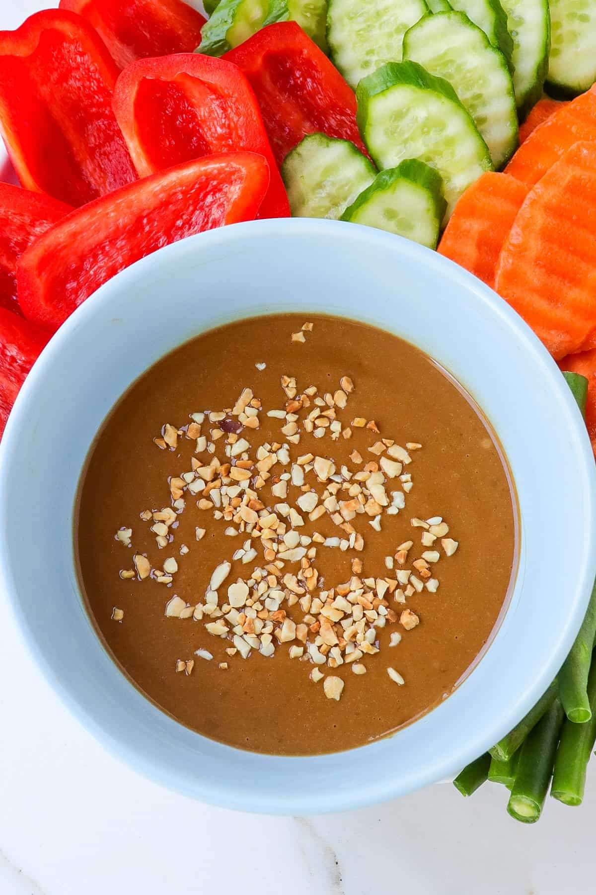 Peanut butter hoisin sauce in a bowl with slices veggies around.