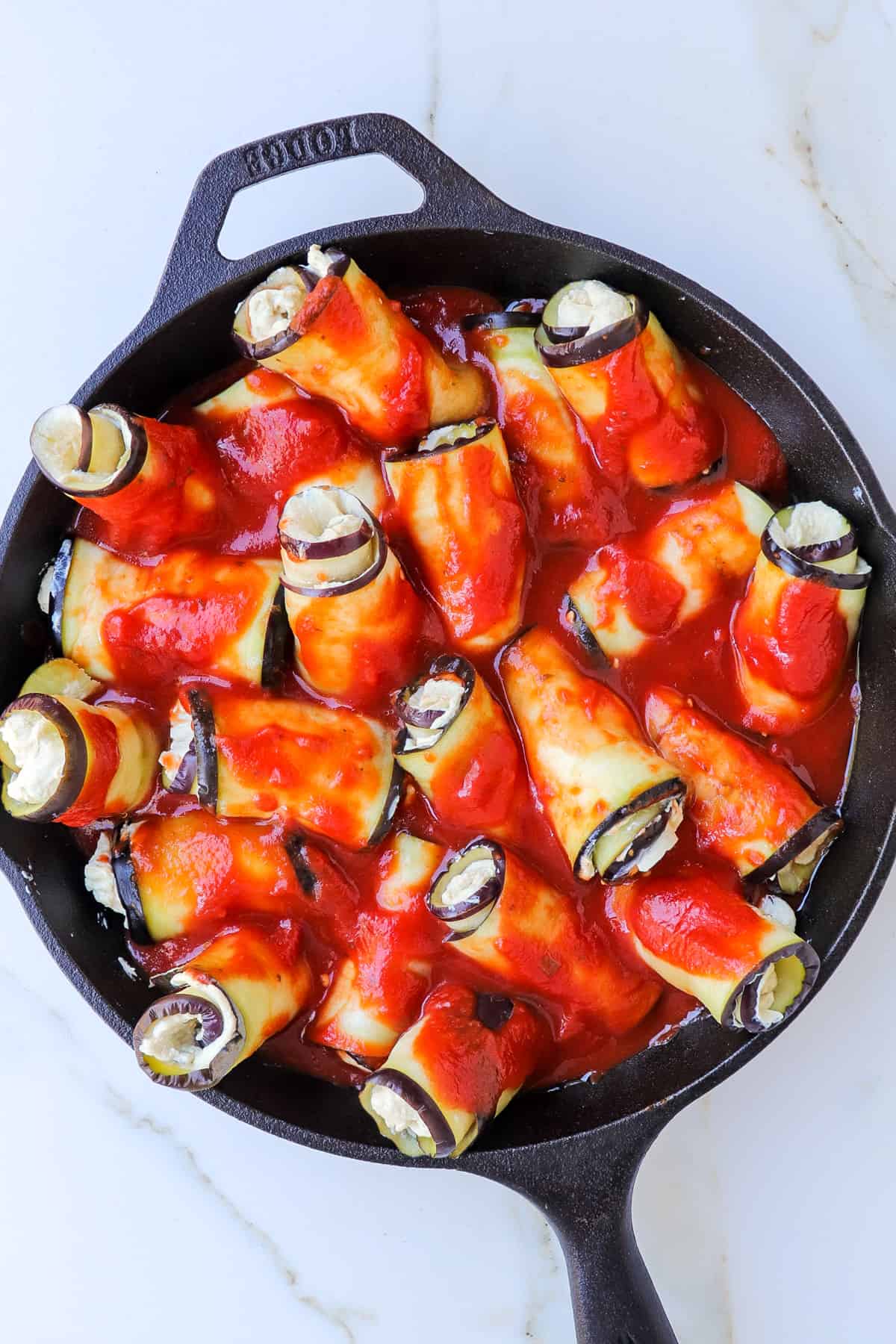 Eggplant rolls in a baking dish with marinara sauce poured on top.