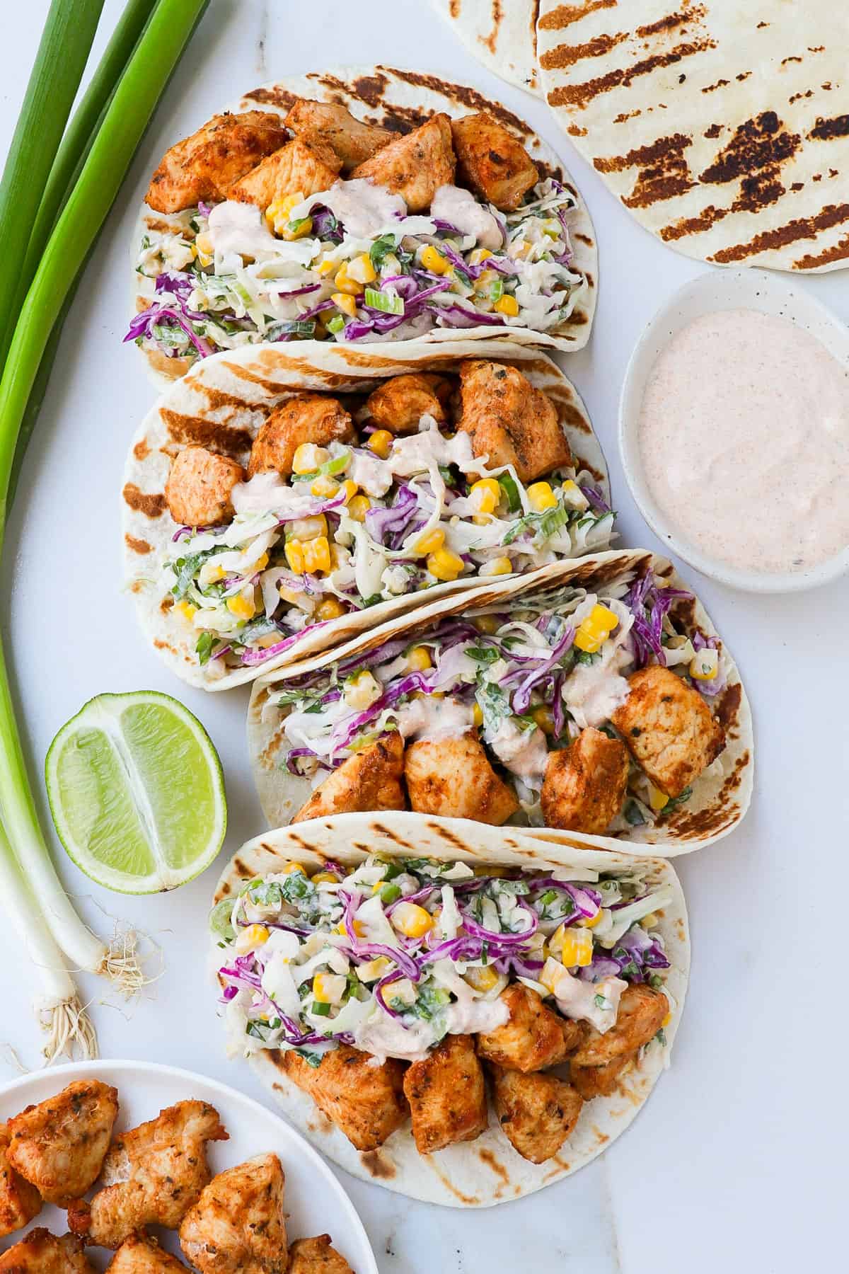 Four air fried chicken tacos with corn slaw with spring onions on the side.