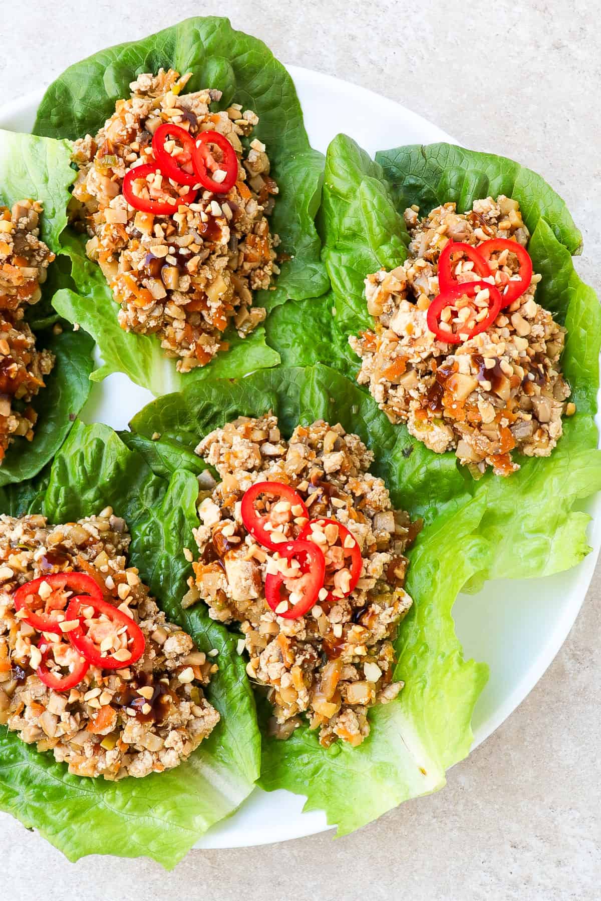 Side shot of vegan lettuce wraps on a plate topped with sliced chilli and crushed peanuts.