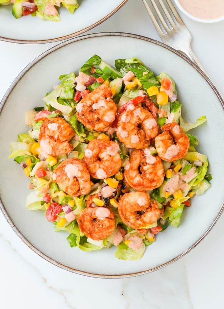 Cajun shrimp salad served in bowls with extra dressing on the side.
