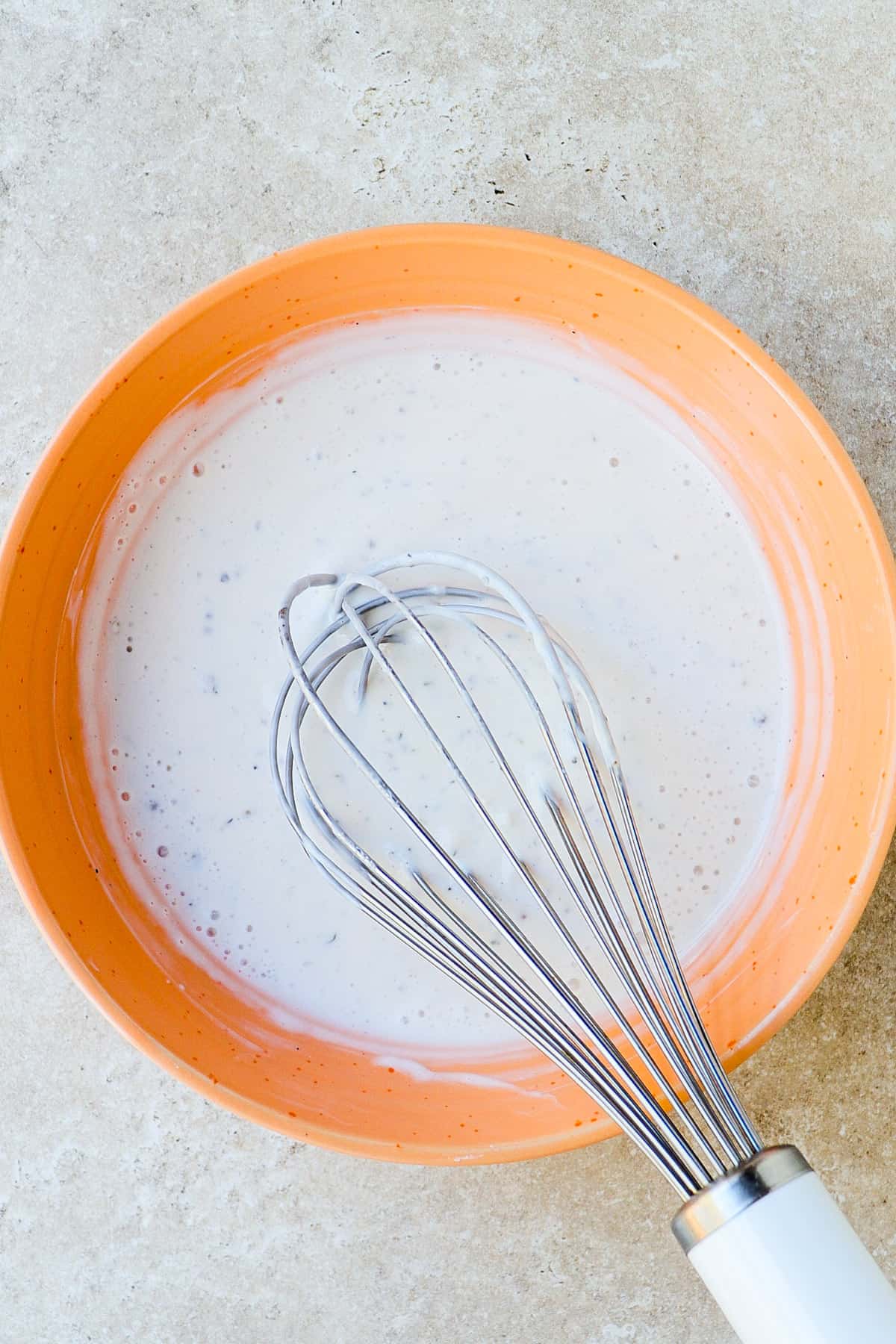 Yoghurt dressing in a orange bowl with a silver whisk.