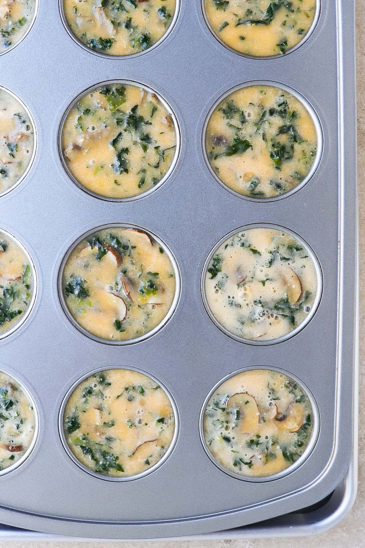 Mushroom, kale and egg mixture in muffin pan on top of a tray to make a steam bath.