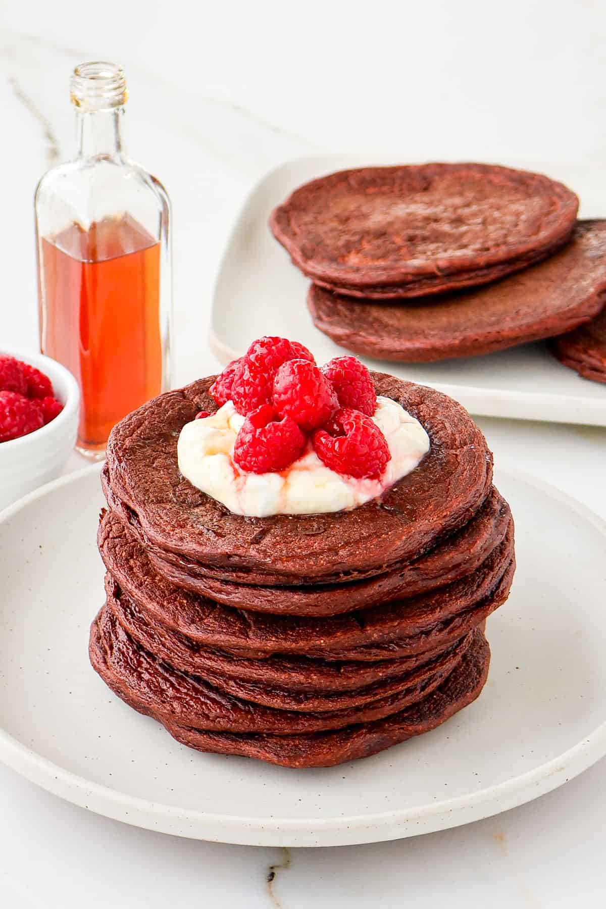 Side shot of chocolate protein pancakes with yoghurt and raspberries on top.