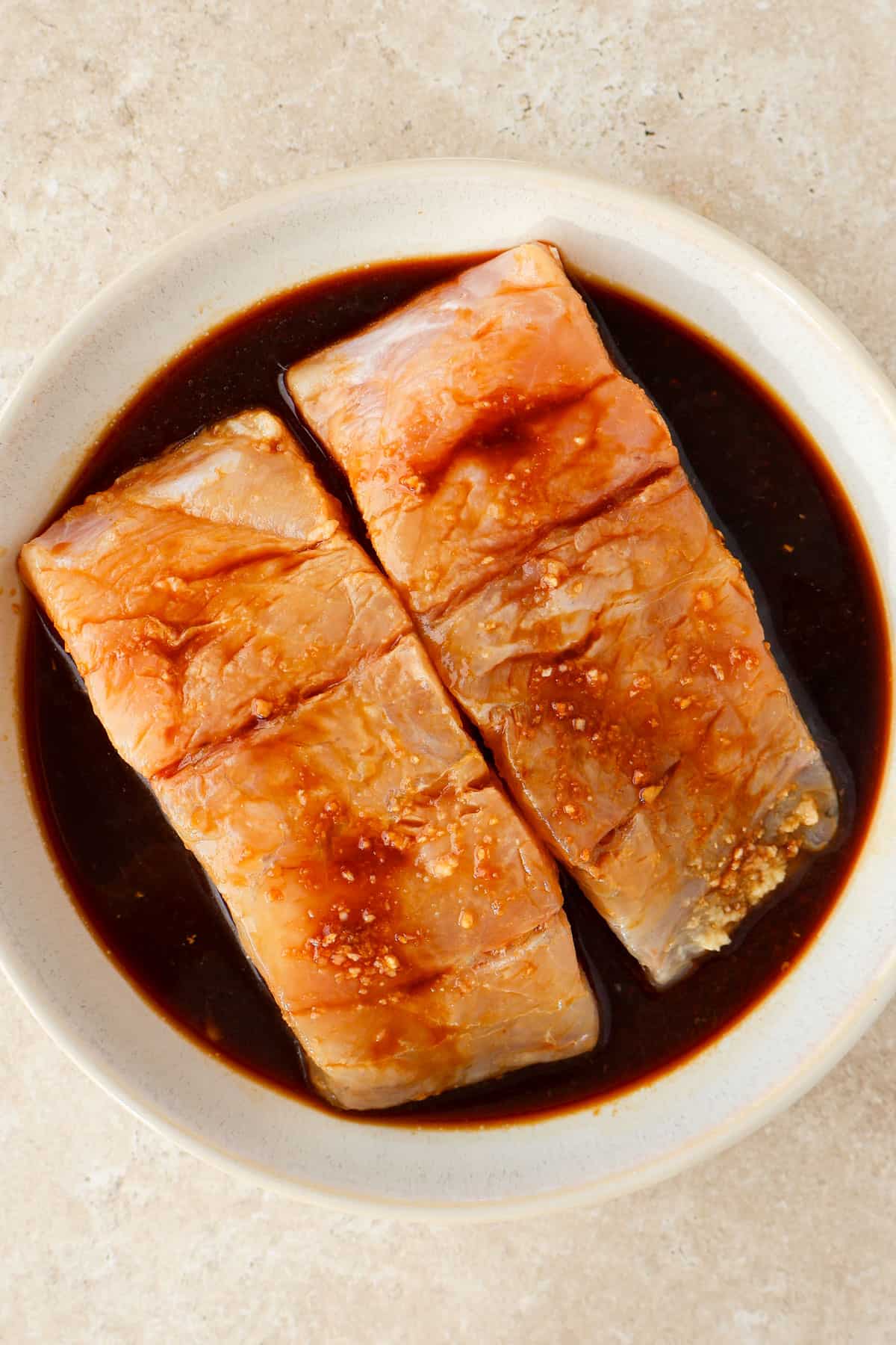 Barramundi fish fillets in a bowl marinating in soy sauce.