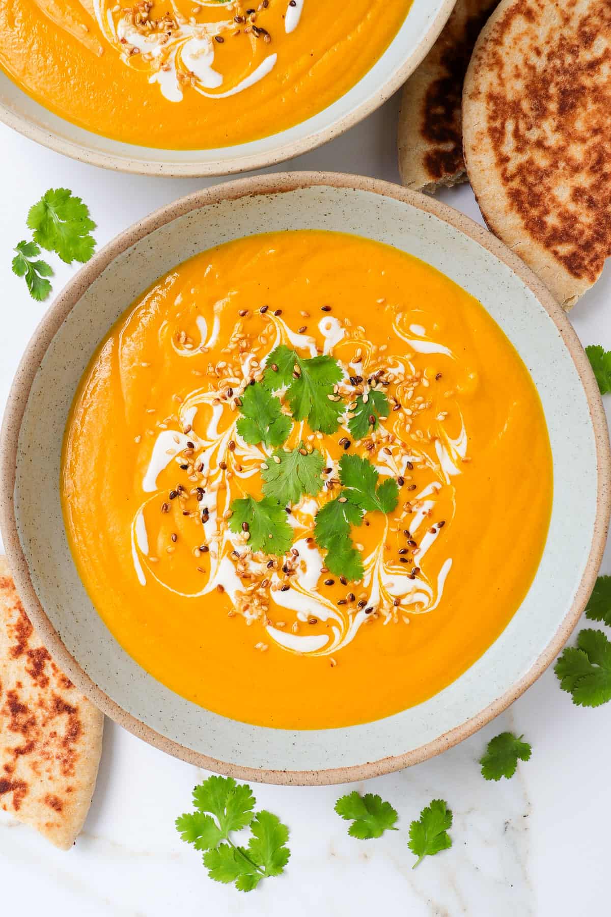 Carrot butterbean soup in a bowl with coriander and tahini swirls. Pita bread on the side.