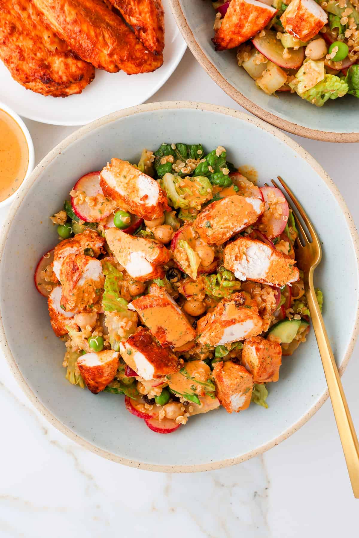 Chicken tikka salad in bowls with a fork and chicken on the side.