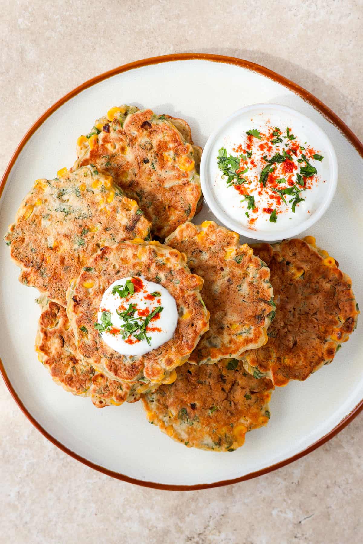Fritters on a plate with yoghurt sauce non the sauce. One topped with paprika yogurt.