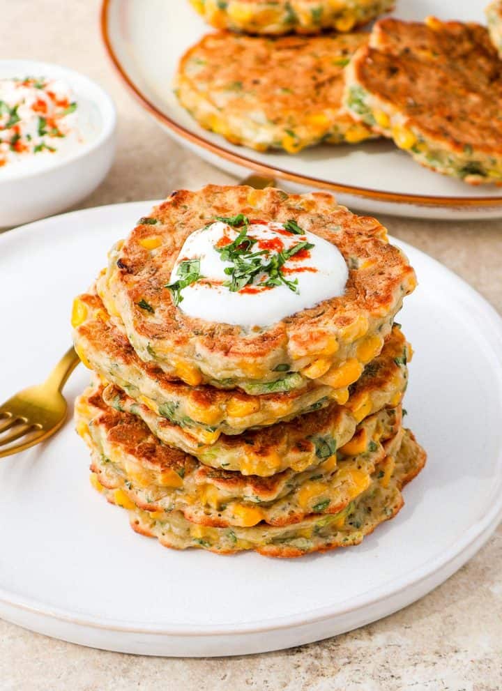 Side shot of corn fritters stacked on a plate.