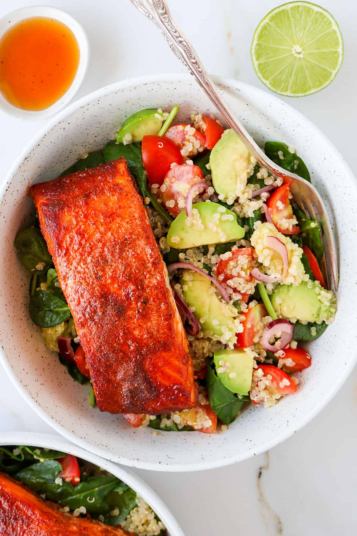 Paprika salmon filet in a bowl with avocado quinoa salad and fork.