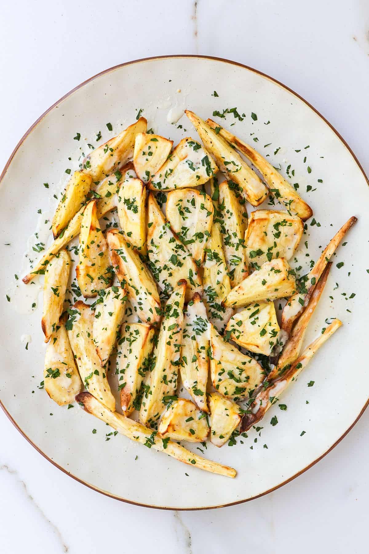 Air fried parsnips on a plate with tahini sauce and parsley.