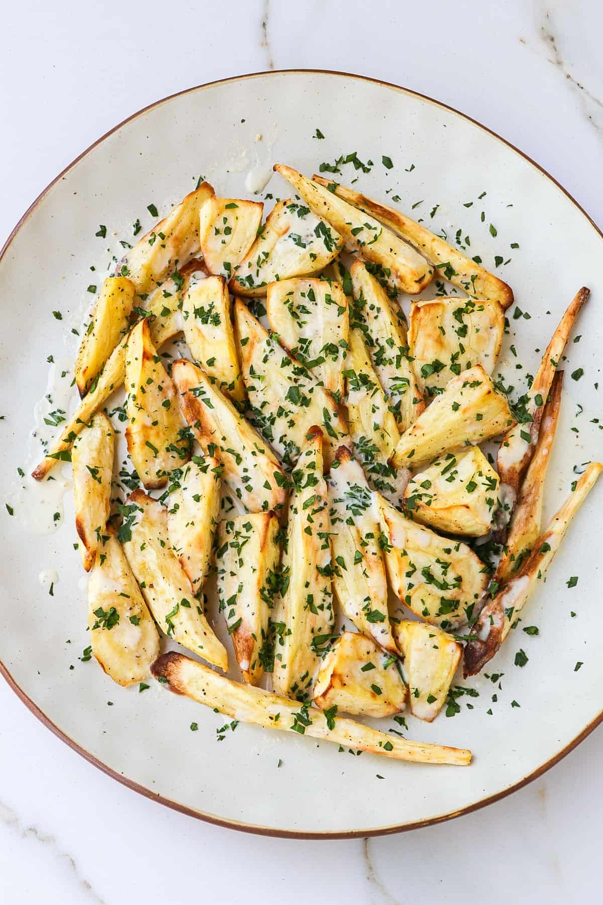 Cooked parsnips on a plate with tahini sauce and parsley.