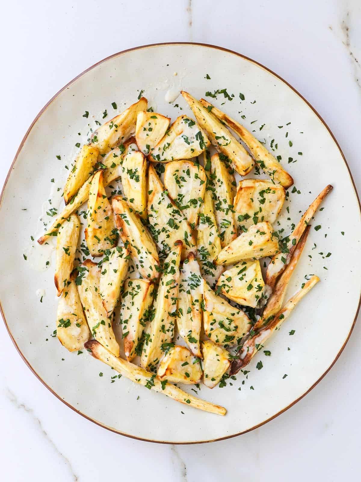 Air fried parsnips on a plate with tahini sauce and parsley.
