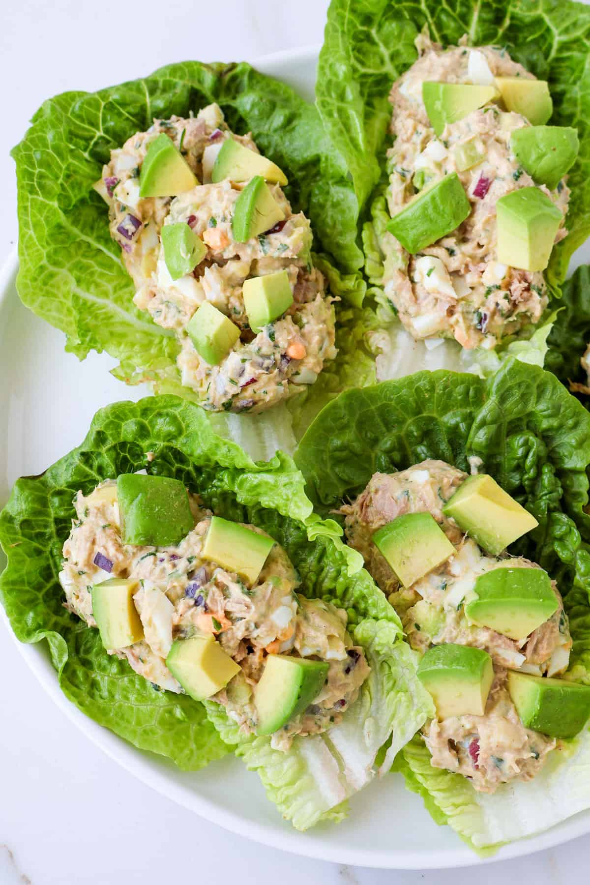 Close up of tuna egg salad in lettuce wraps with avocado chunks on top.