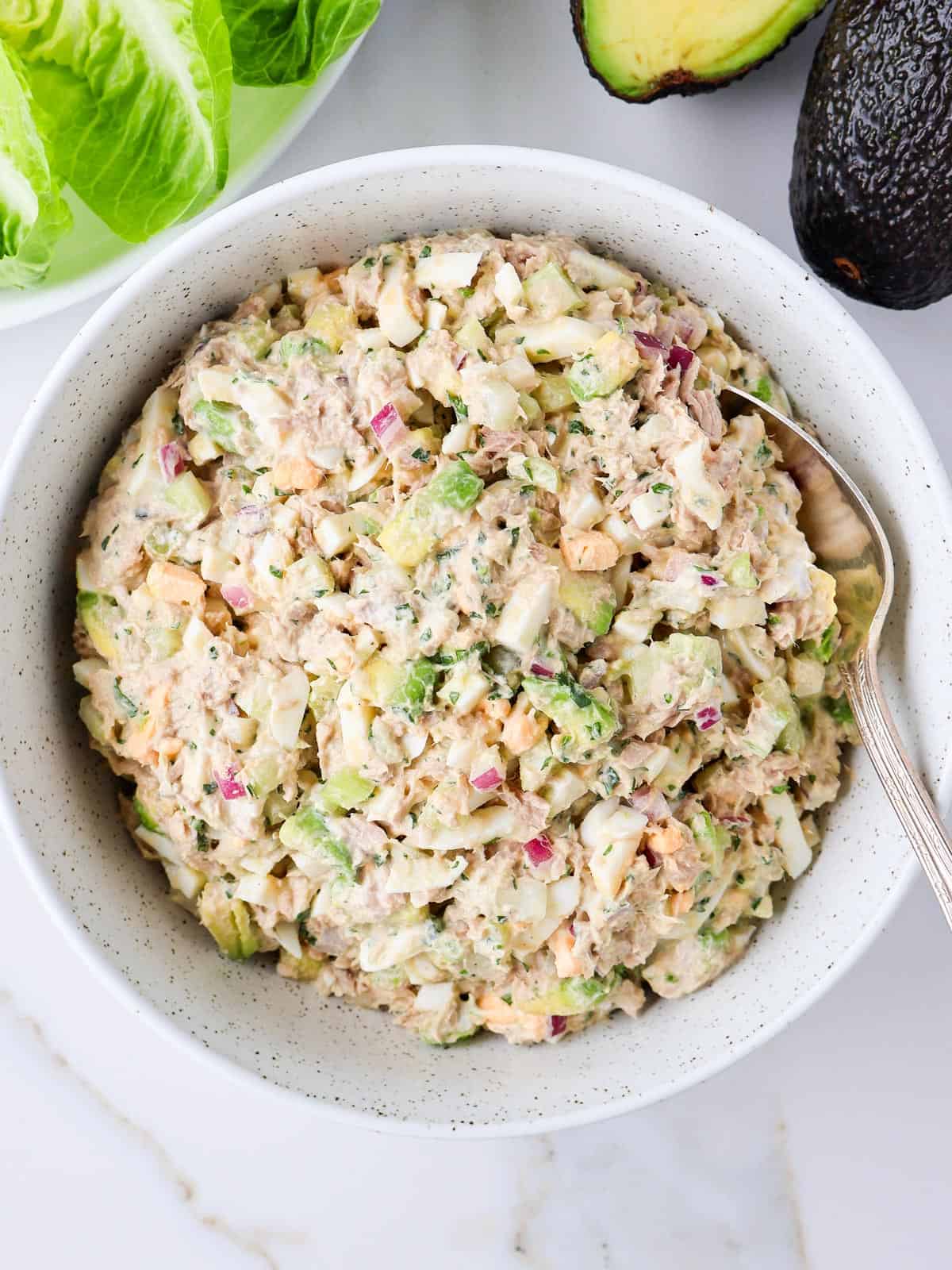Tuna avocado salad egg salad in bowl with a spoon.