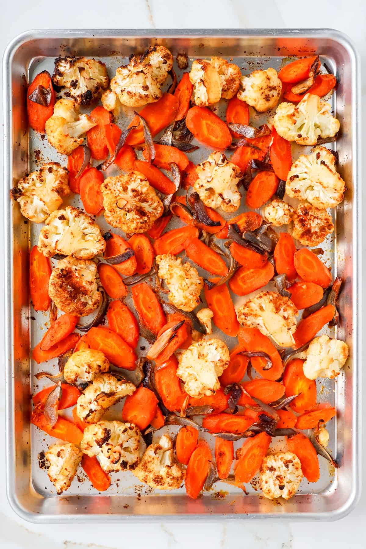 Roasted cauliflower, carrots and onions on a baking sheet.