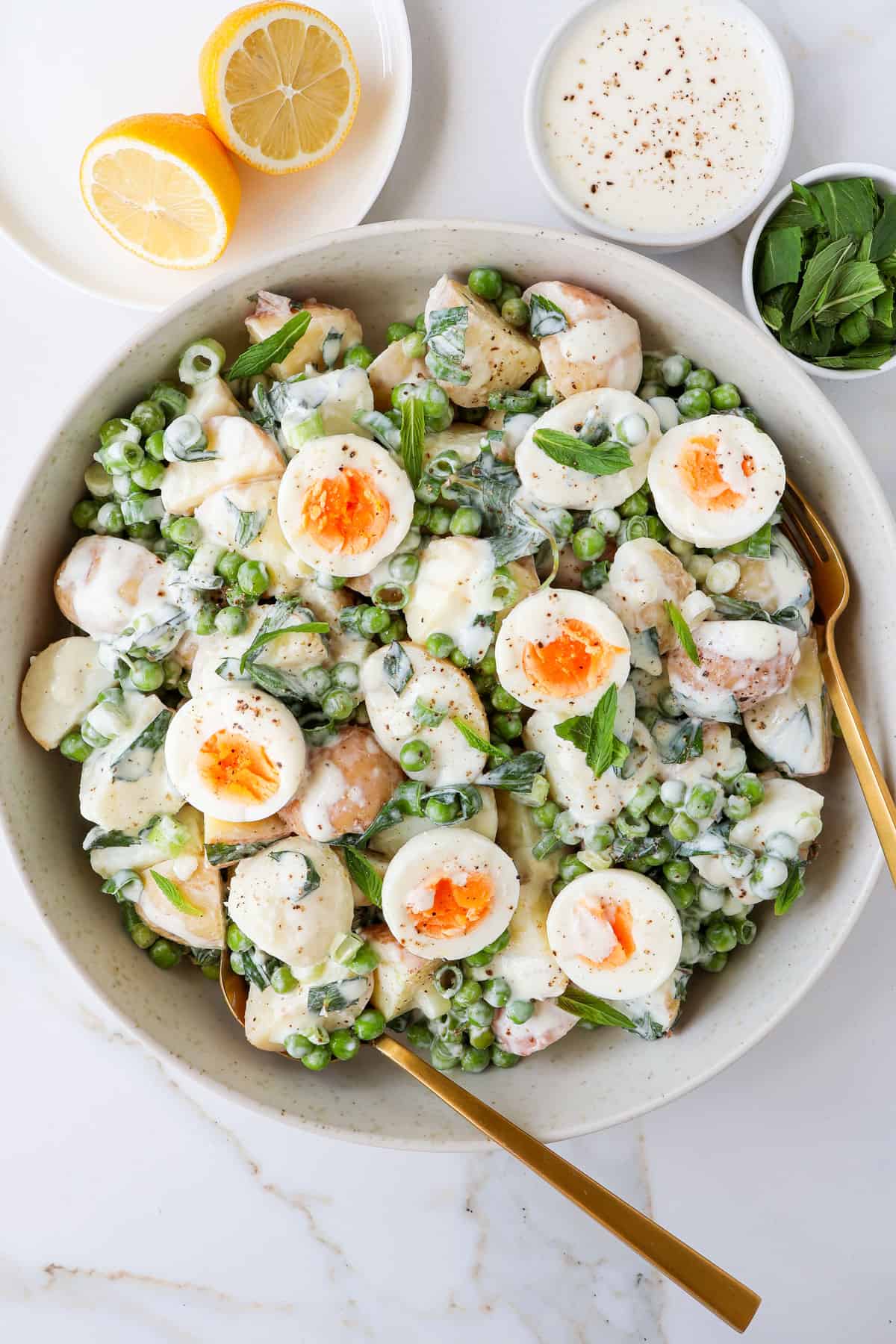 Spring onion potato salad in a bowl with mint and hard boiled eggs on top.