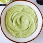 Crema in a bowl with an avocado on the side.