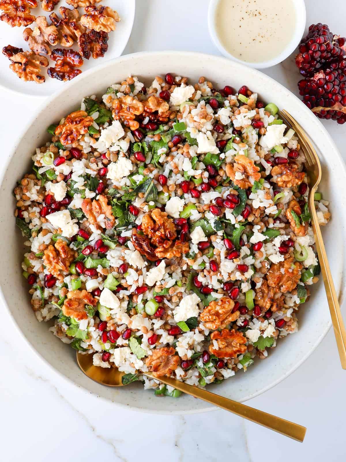 Pomegranate and walnut salad in a bowl with serving spoons.