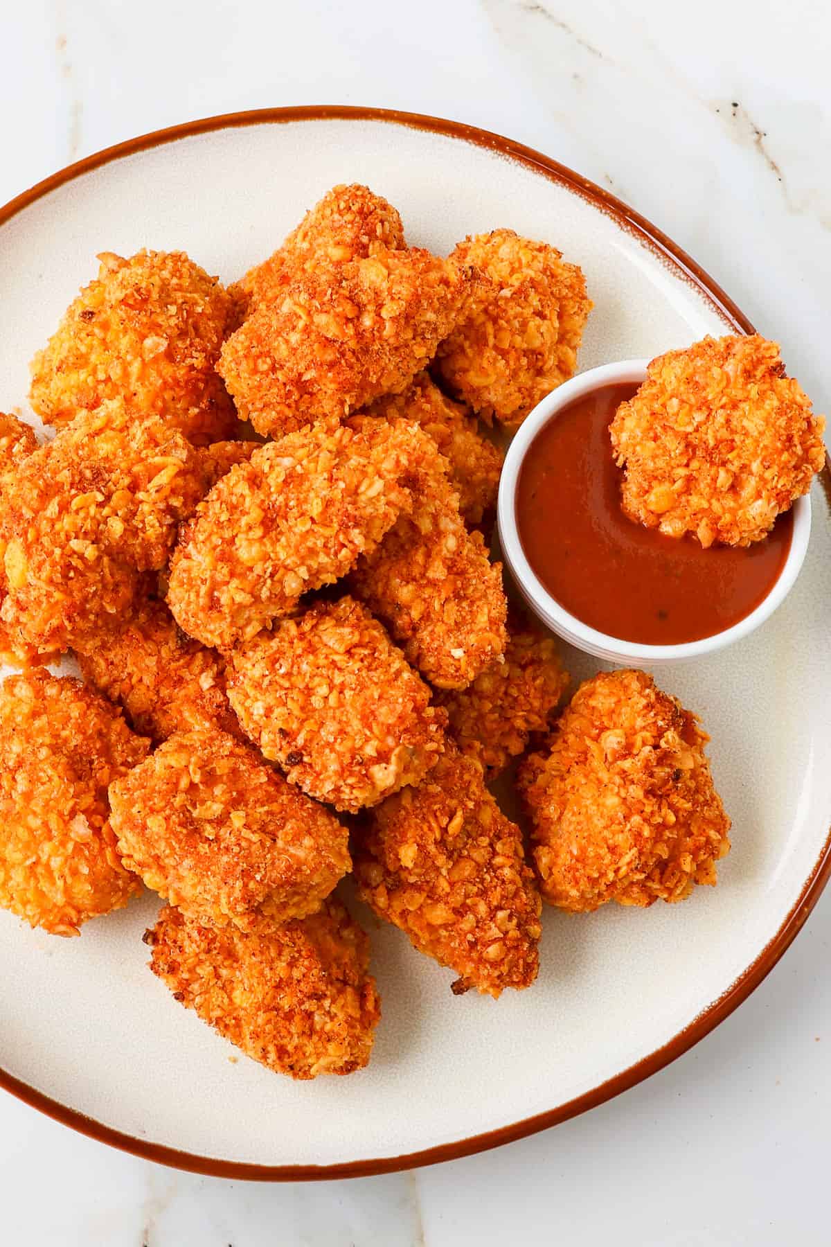 Close up shot of cornflake chicken nuggets dipped into bbq sauce.