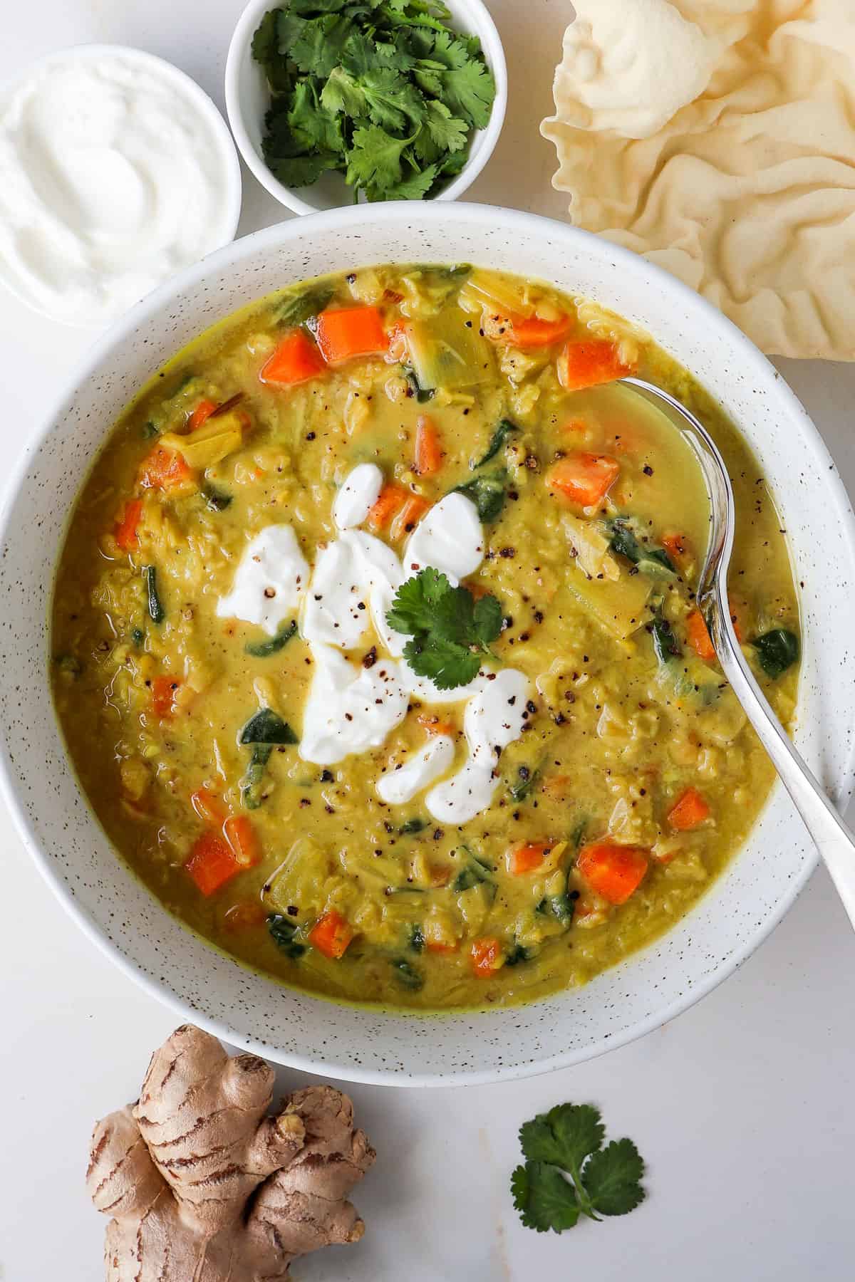 Carrot and lentil soup in a bowl topped with yoghurt and a spoon.