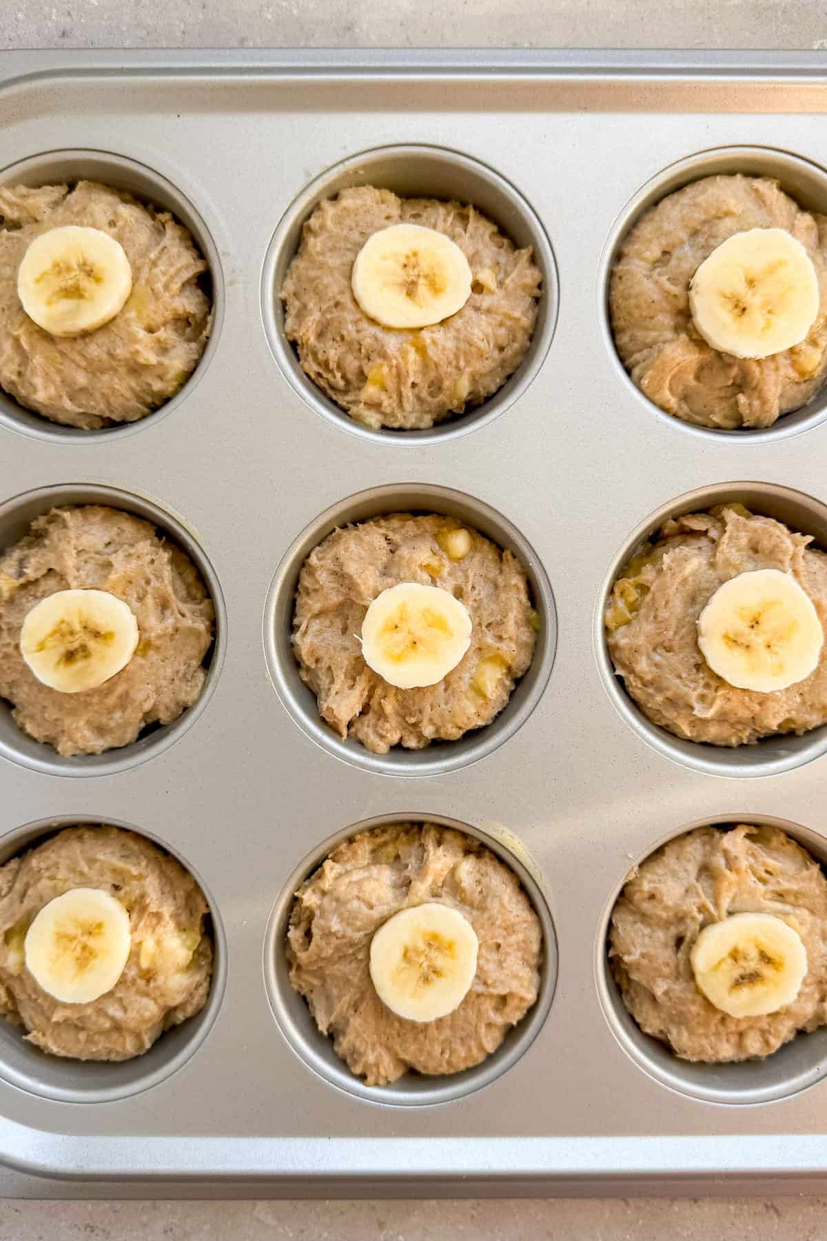 Batter added to muffin pans with banana slice on top.