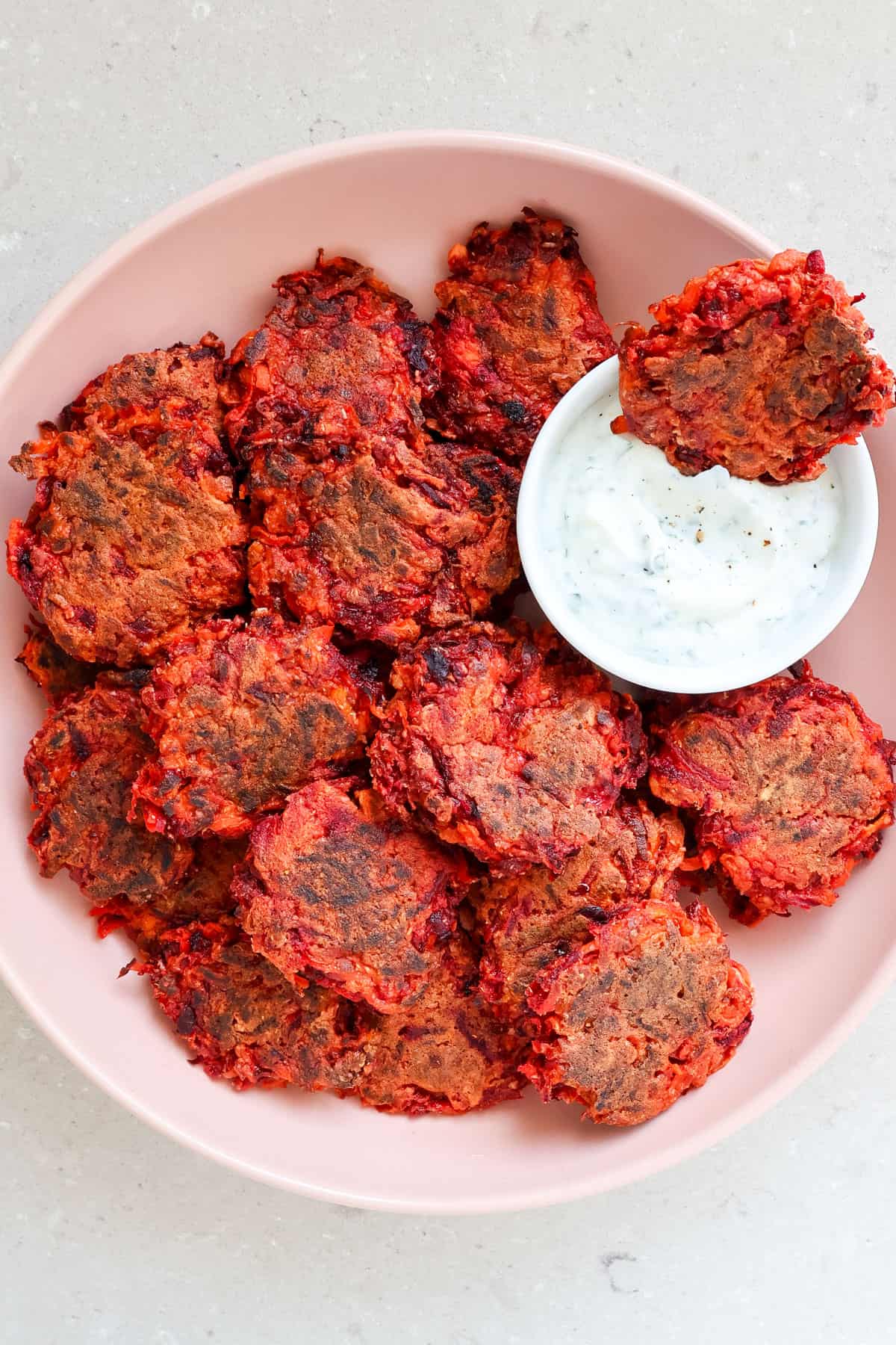 Beetroot fritters in a bowl dipped in yoghurt sauce.