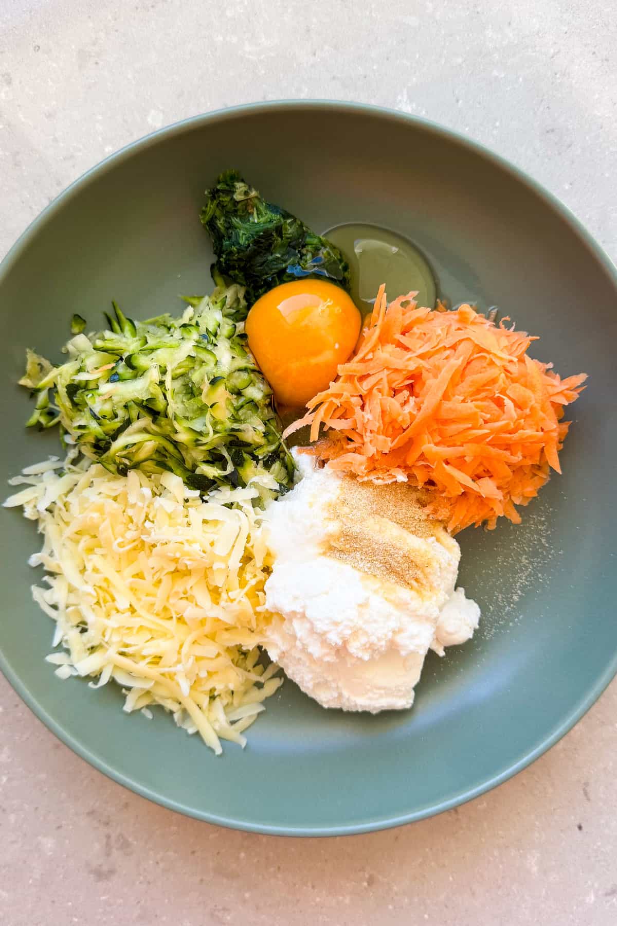 Grated veggie, cheese, ricotta and egg being mixed in a bowl.