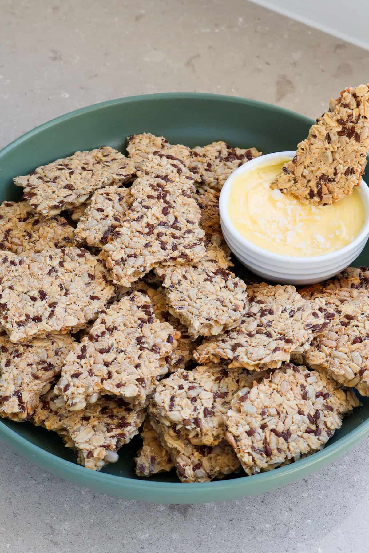 Side shot of oatmeal sunflower seed crackers in a bowl dipped in salted butter.