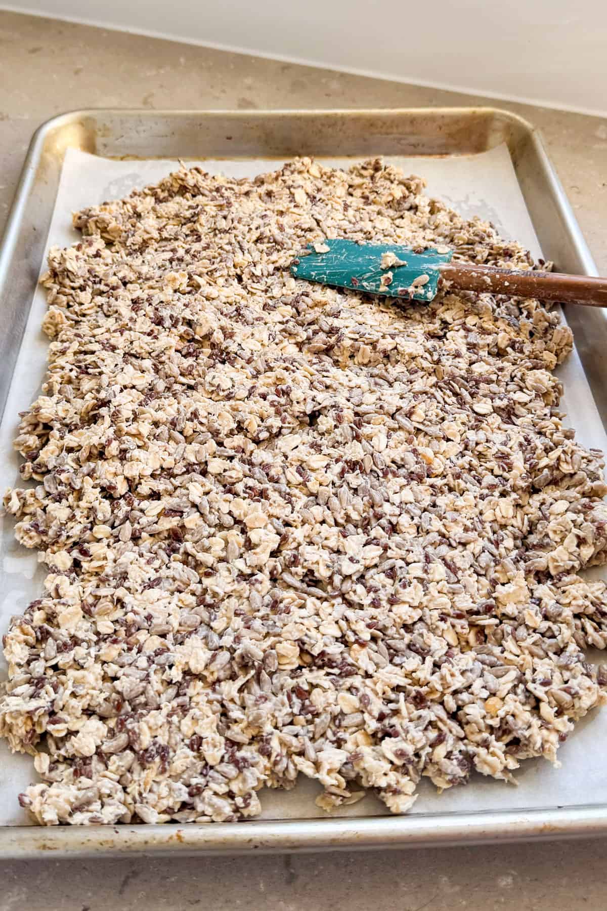 Seed mixture spread on baking tray with spatula.
