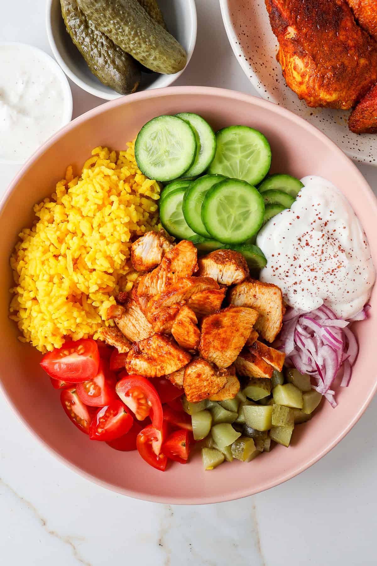 Chicken shawarma rice bowls with cucumbers, tomatoes, pickles, onions and yogurt sauce.