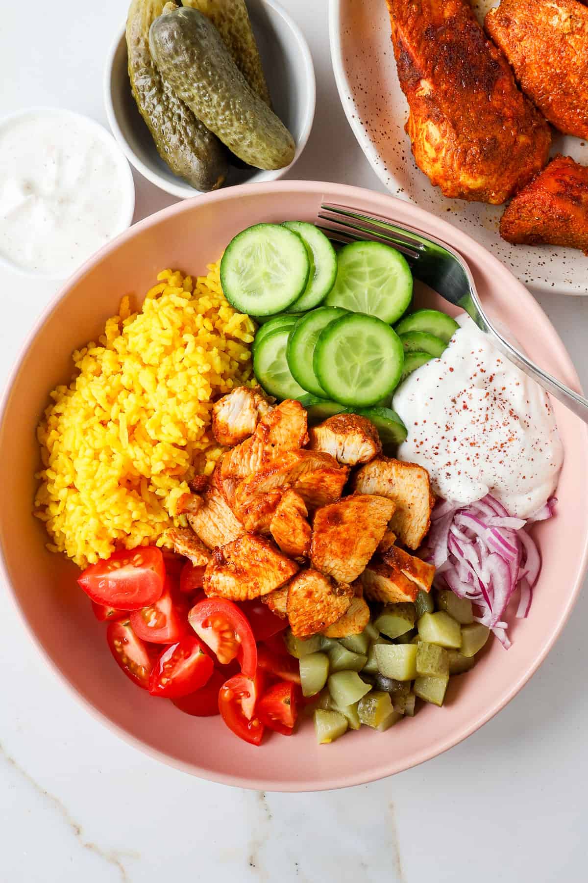 Chicken shawarma in a bowl with turmeric rice, veggies, pickles, and yogurt sauce.