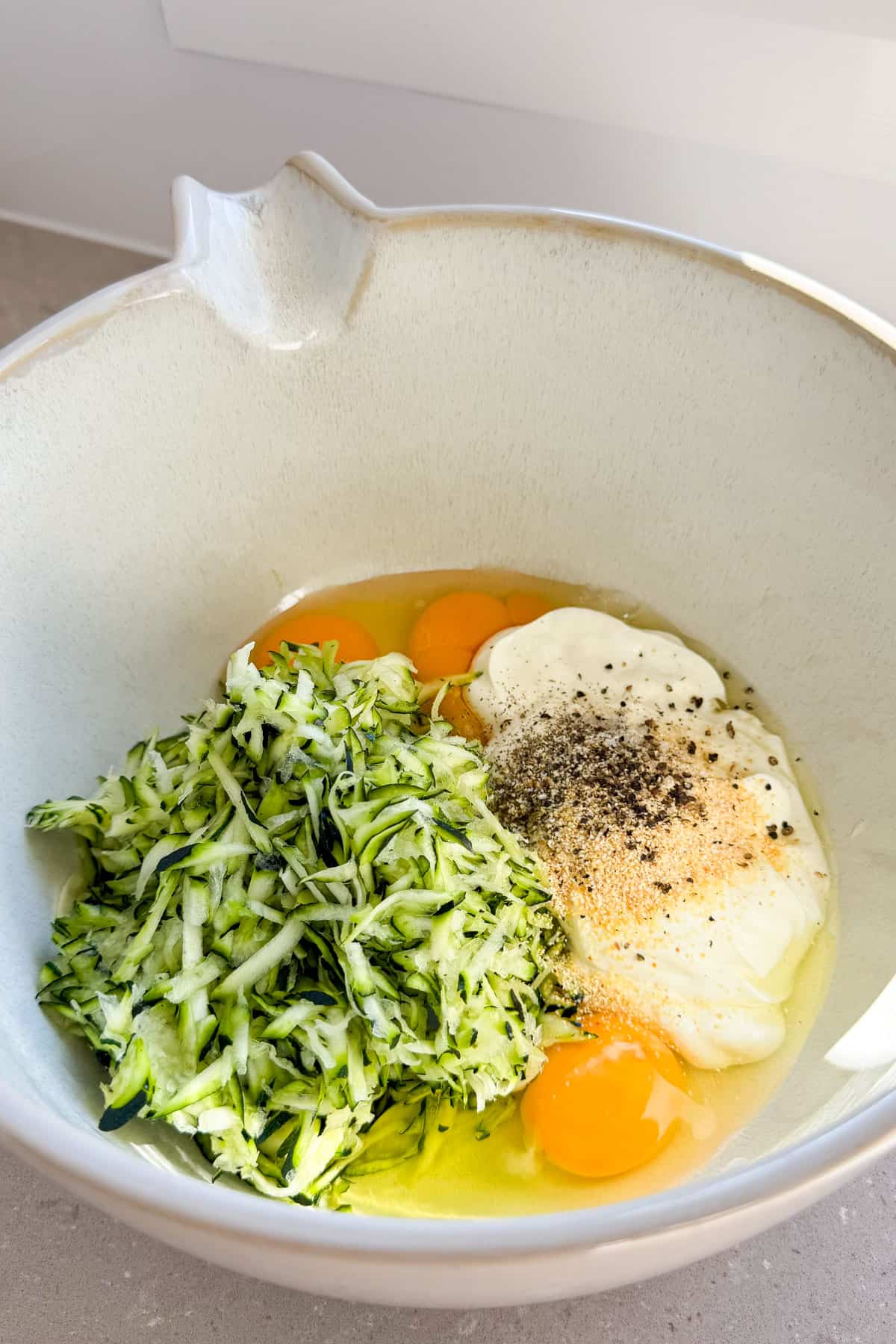 Zucchini, eggs, yogurt and seasonings in a mixing bowl.