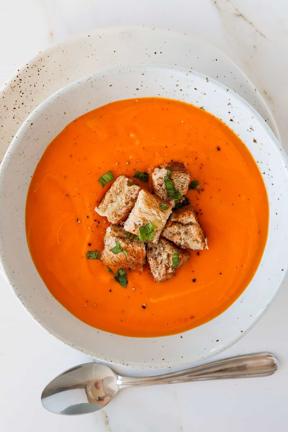 Butternut squash tomato soup in a bowl with grilled cheese and a spoon.