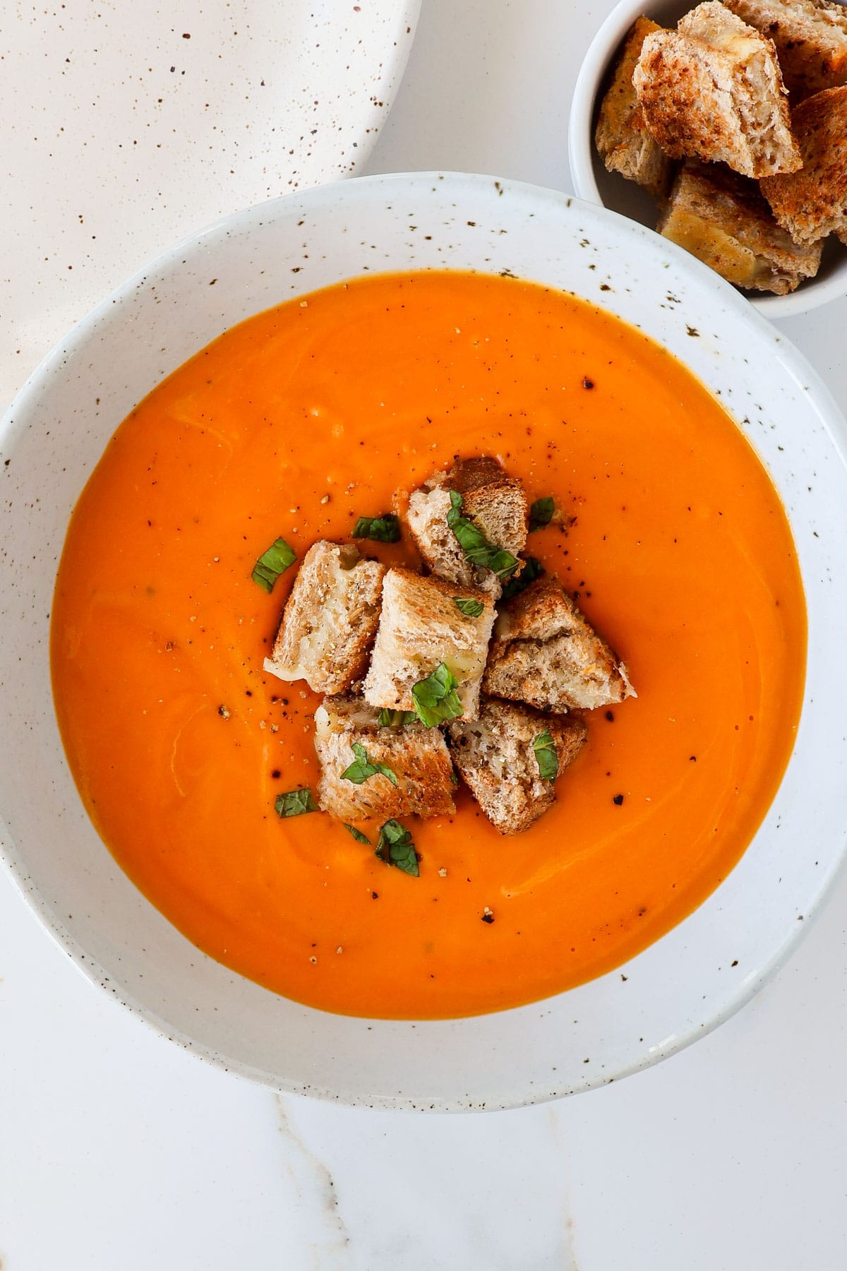Tomato butternut squash soup in a bowl with grilled cheese on top and the side.