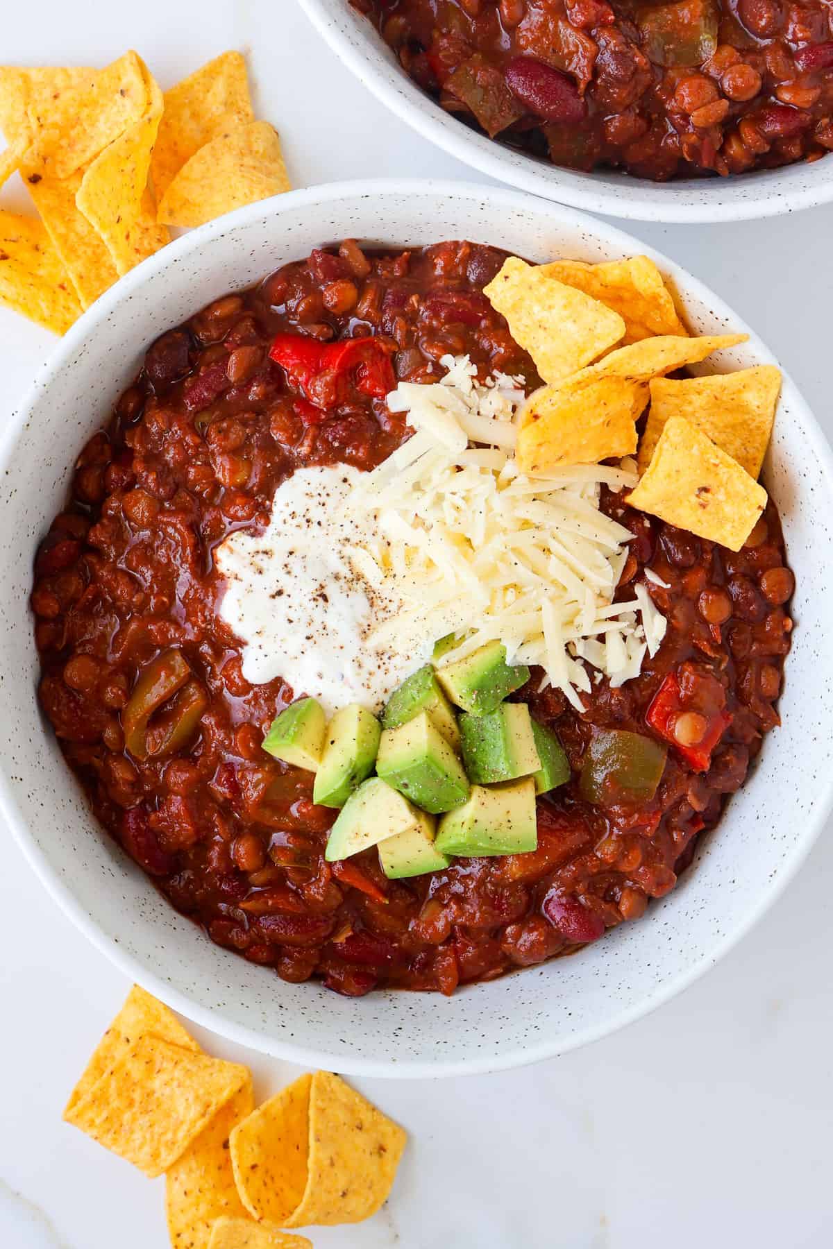 Lentil chili in bowls with yogurt, avocado cheese and tortilla chips on top.