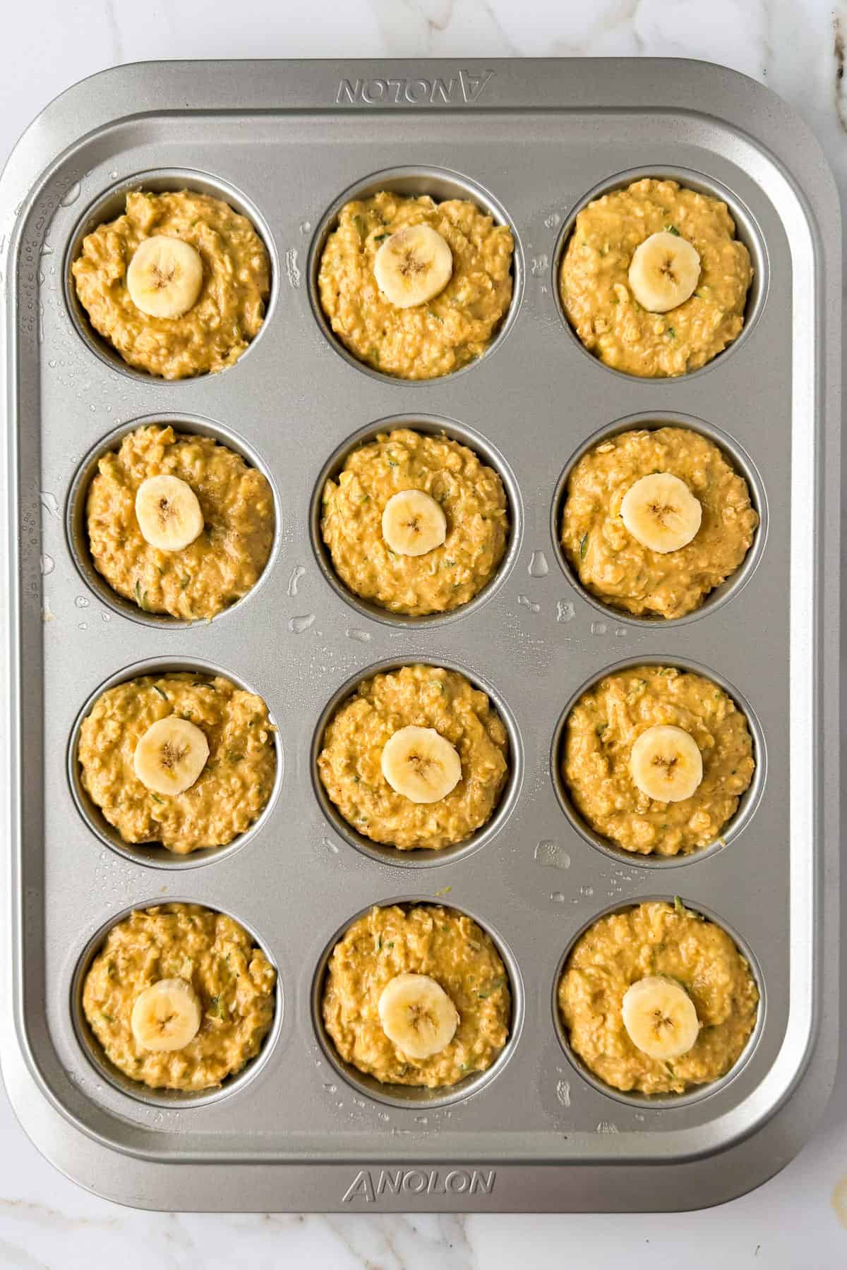 Muffin batter added to muffin pans and topped with a banana coin.
