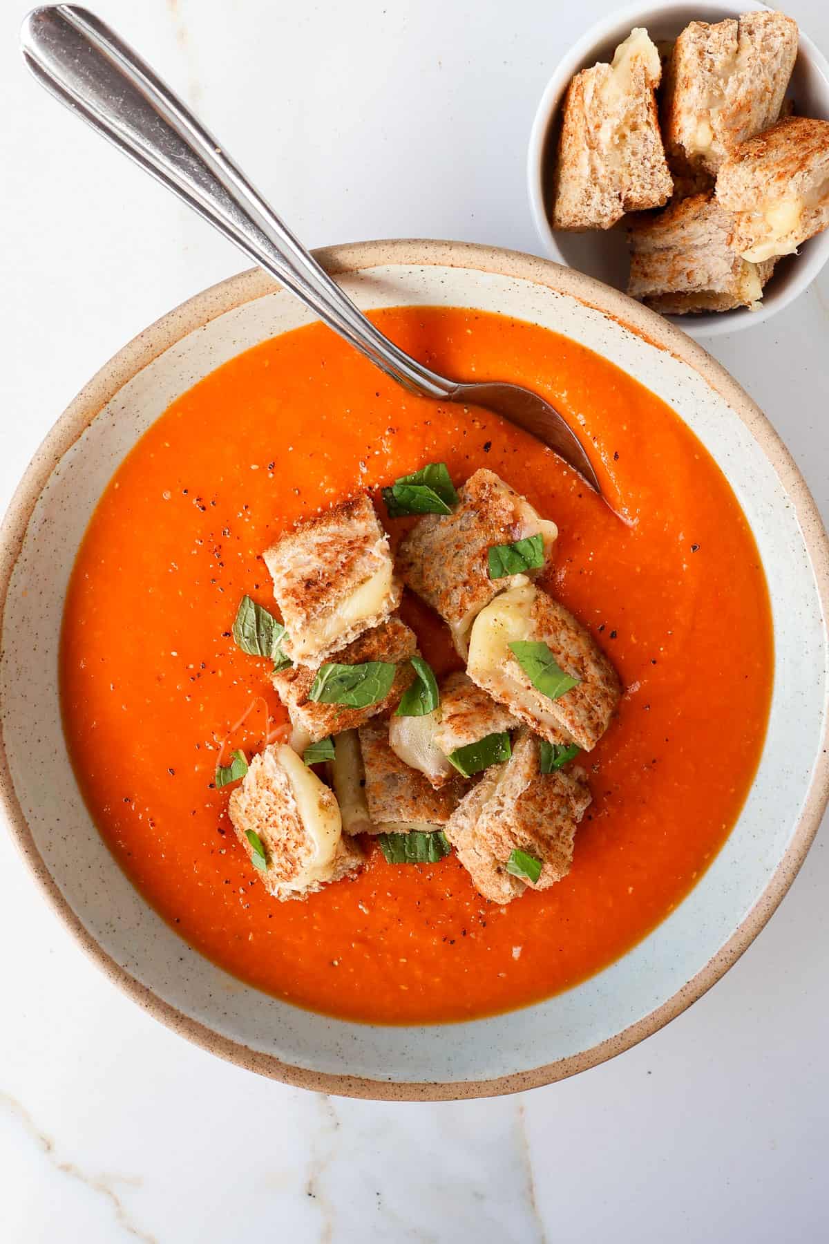 Soup in a bowl with a spoon and grilled cheese croutons on the side.