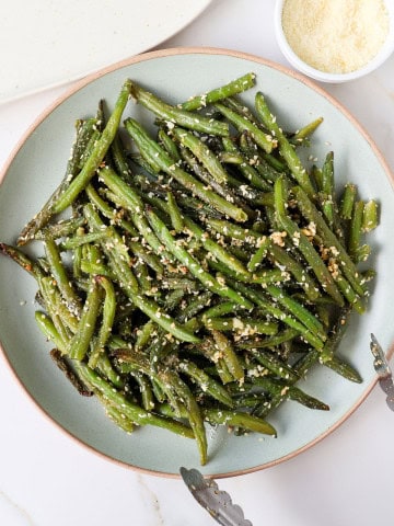 Roasted green beans on a plate with tongs.