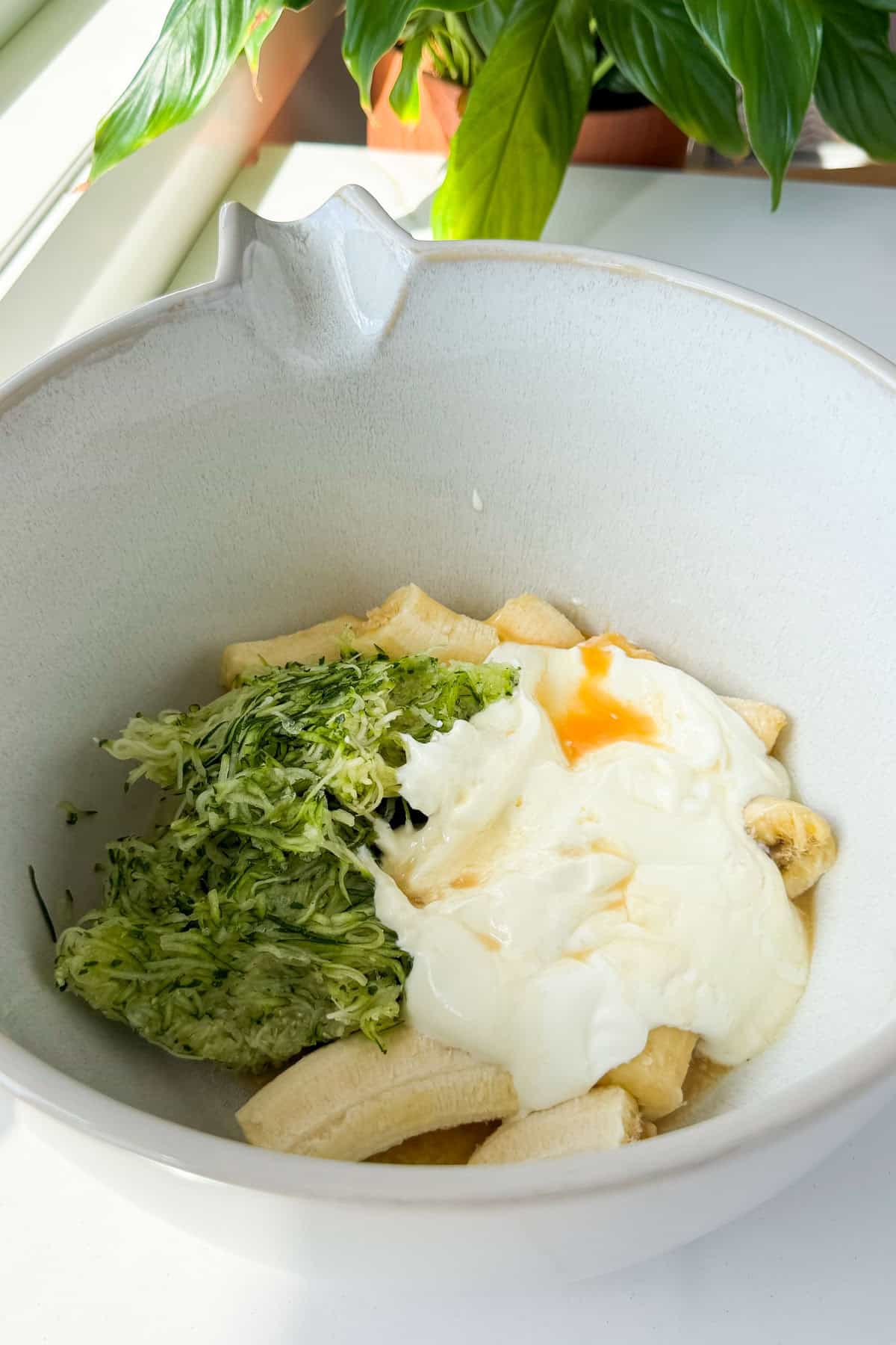 Bananas, zucchini, yoghurt and egg added to a bowl.