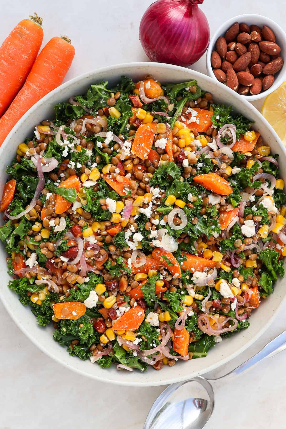 Kale and lentil salad in a bowl with corn, carrots feta crumbled on top.