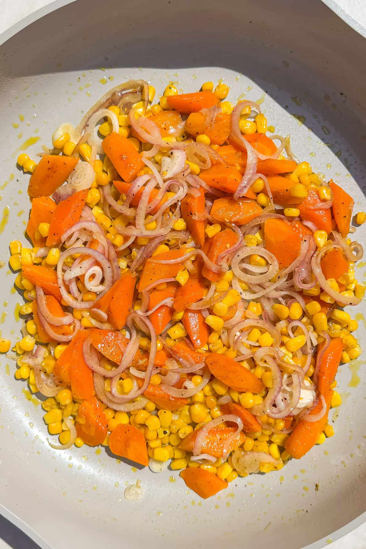 Sautéed carrots, corn and onions in a pan.