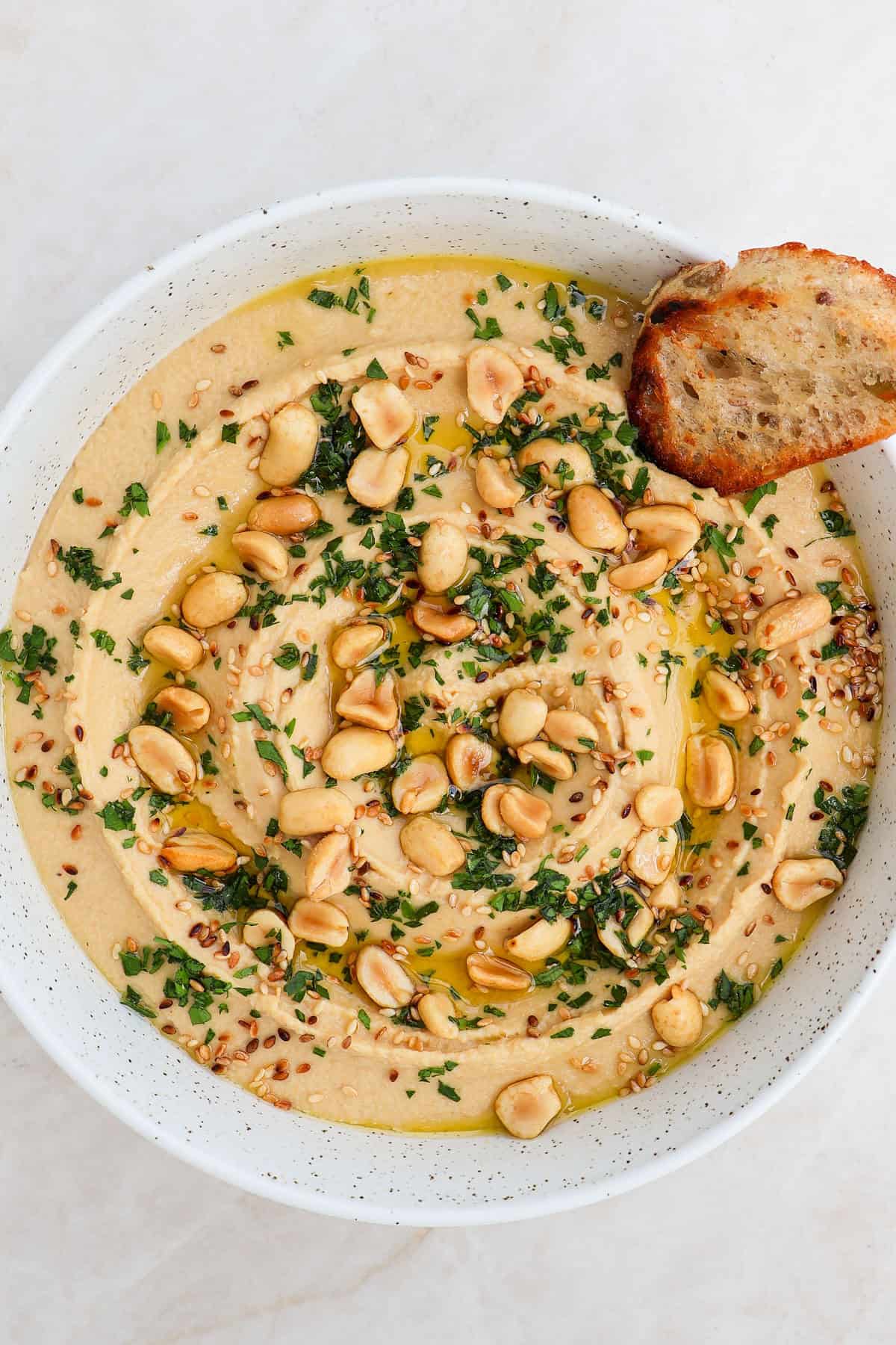 Peanut hummus in a bowl with crostini dipped in.