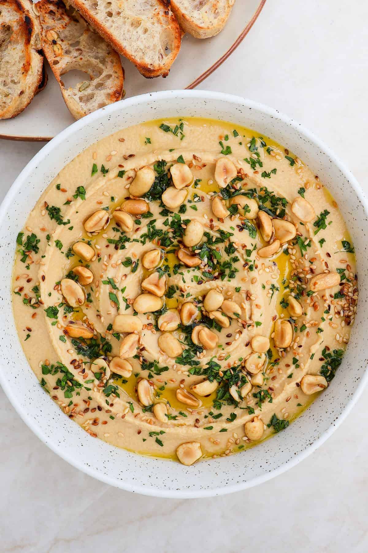 Peanut hummus in a bowl topped with peanuts, herbs, sesame seeds and crostini on the side.